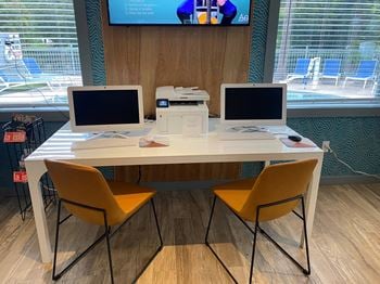A desk with two computers on it and a tv in the background